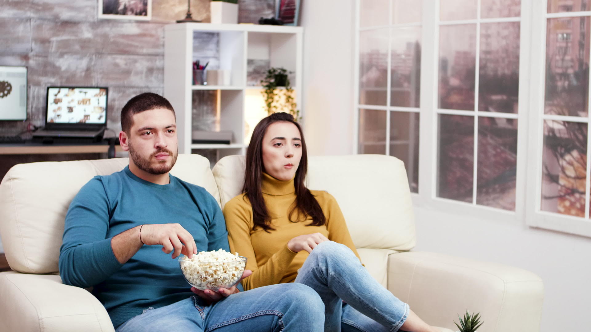 年轻夫妇笑着看着电视坐在沙发上视频的预览图
