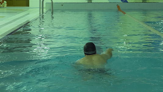 戴着帽子和护目镜的运动员在游泳池里爬上蓝色的水视频的预览图