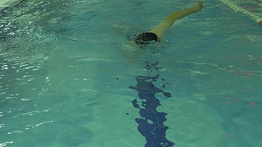 戴着帽子和护目镜的运动员正在游泳池里爬行蓝水冲向游泳池视频的预览图