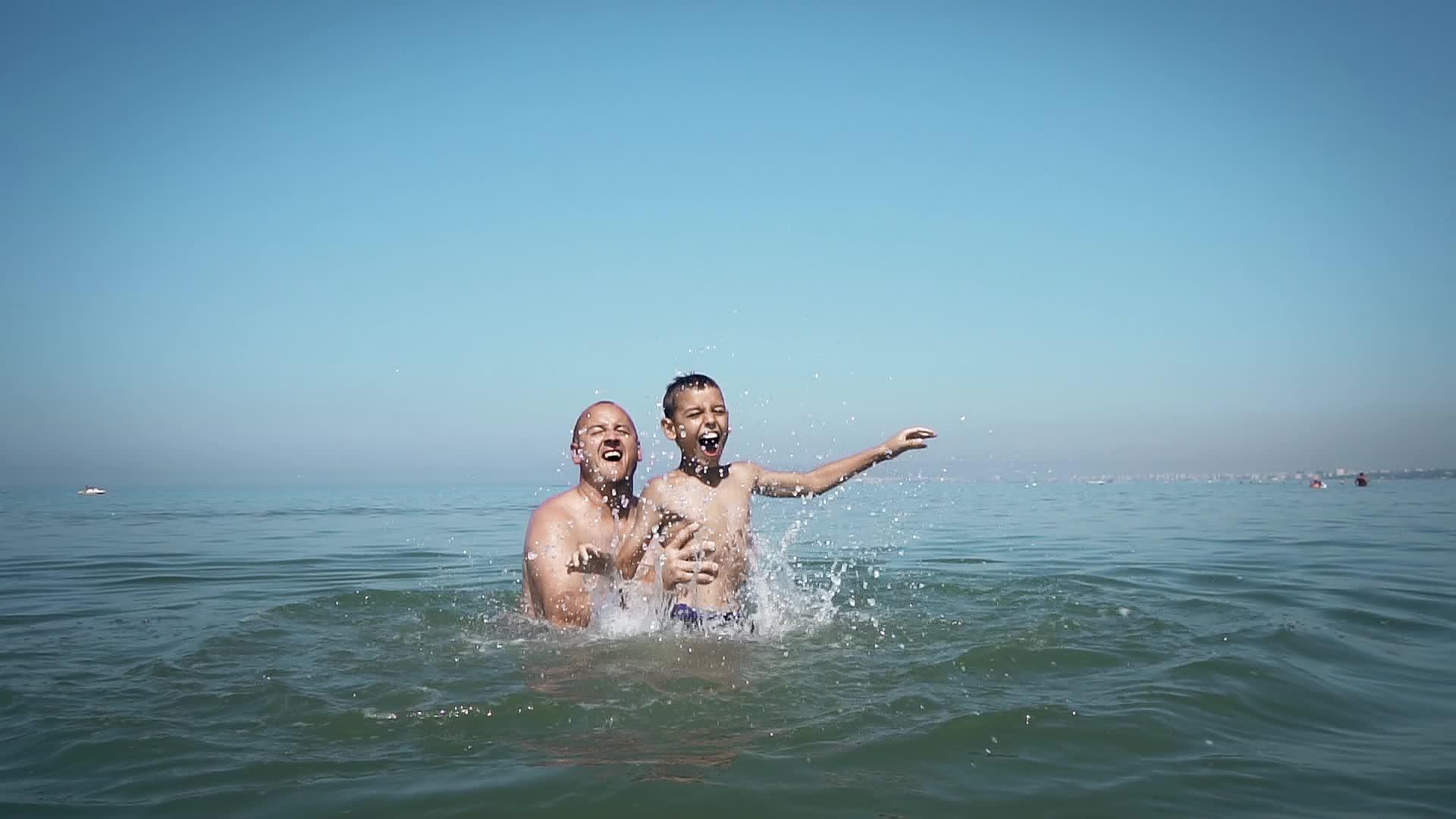 快乐的父子家庭在海滩上的海水中投掷跳跃和玩耍——慢动作视频的预览图
