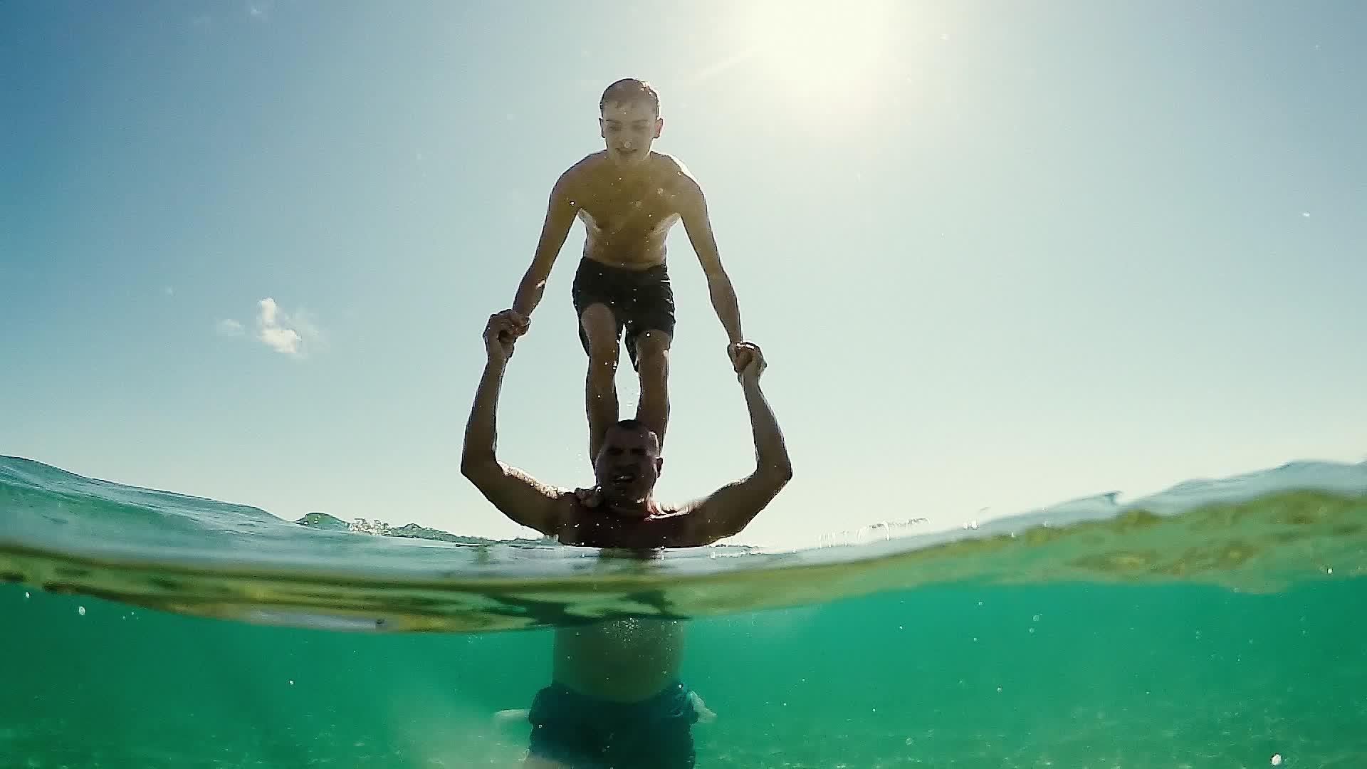这个年轻的男孩从站在父亲的肩膀上掉进了水里地球圆顶半水下视频的预览图