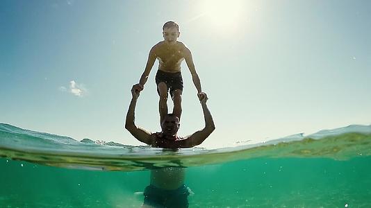 这个年轻的男孩从站在父亲的肩膀上掉进了水里地球圆顶半水下视频的预览图