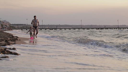 父亲和儿子带着球在海滩上奔跑视频的预览图