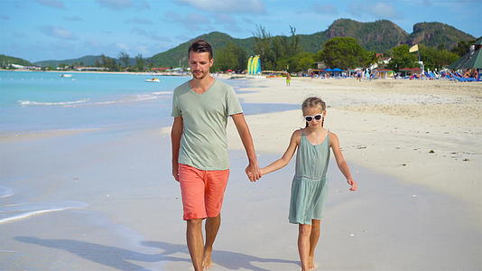 快乐的父亲和他可爱的小女儿在热带海滩散步视频的预览图