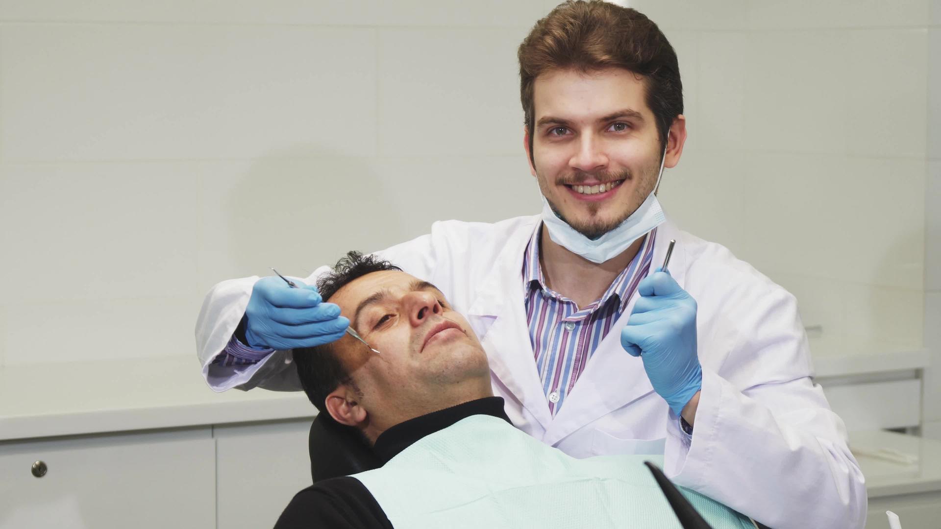 年轻的男性牙医在牙科检查病人时微笑着视频的预览图