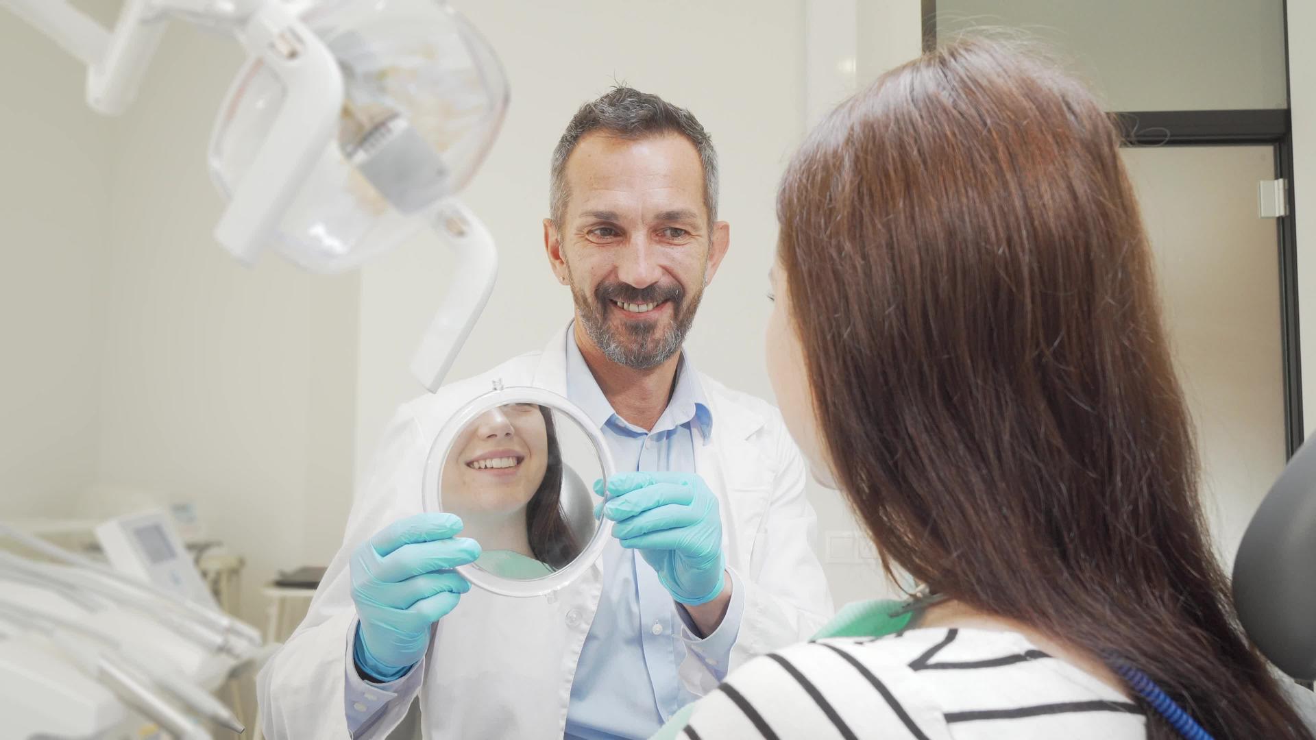 快乐成熟的牙医为他的女病人拿了一面镜子视频的预览图