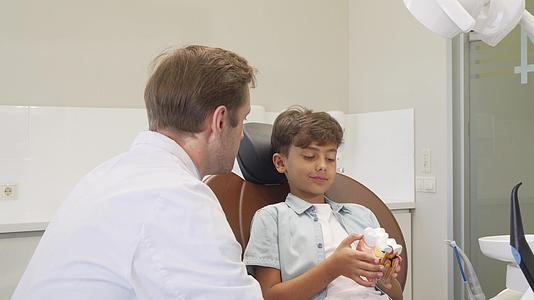 和可爱的小男孩一起工作时成熟的牙医对着镜头微笑视频的预览图