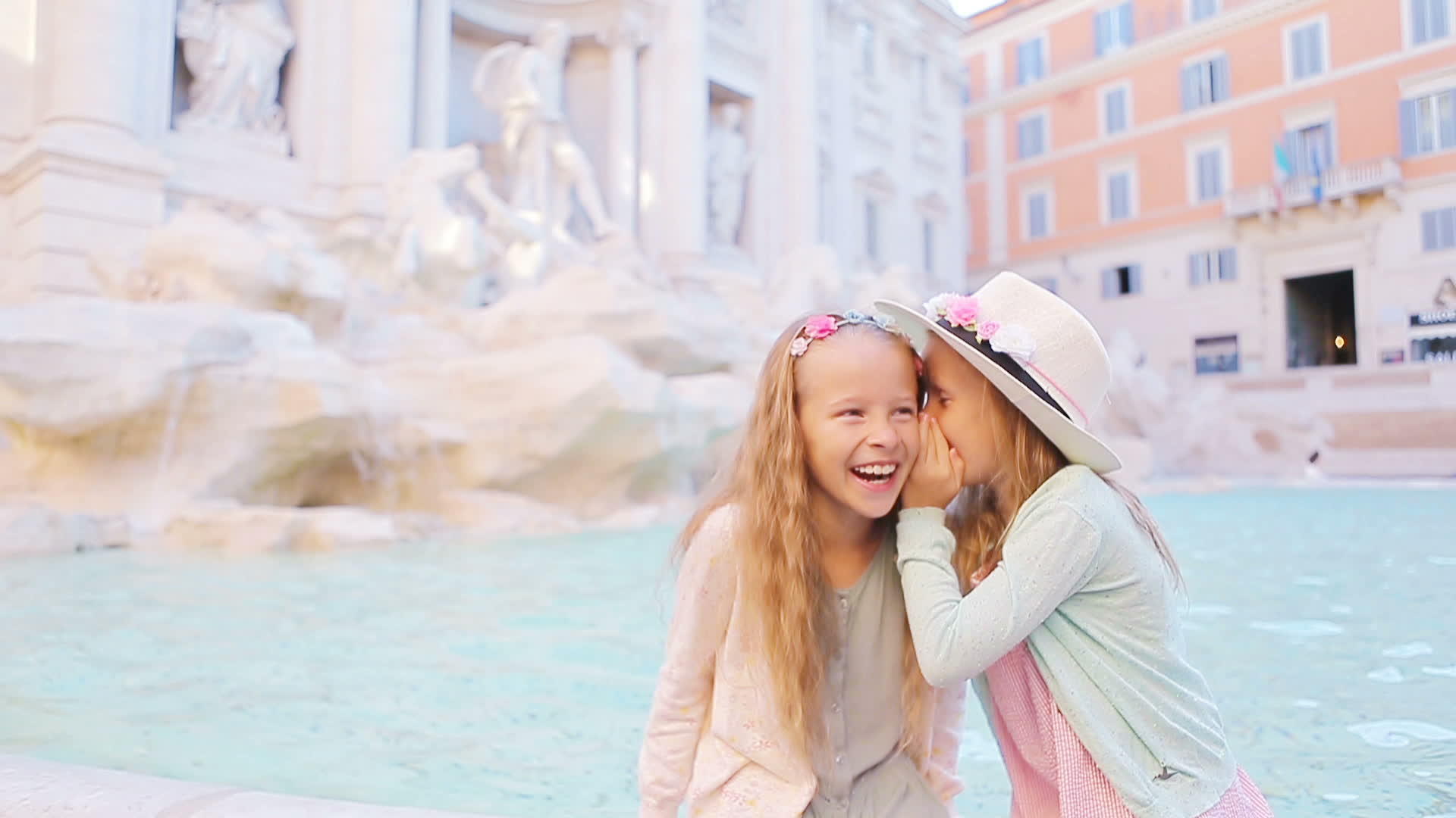 可爱的小女孩坐在罗马特莱维喷泉的边缘窃窃私语快乐地低语视频的预览图