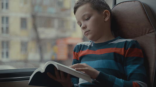 一名年轻的男中学生乘公共汽车穿过城市读了一本书视频的预览图