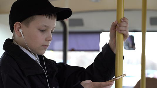 一个男孩乘公共汽车在城里旅行他用智能手机听音乐视频的预览图
