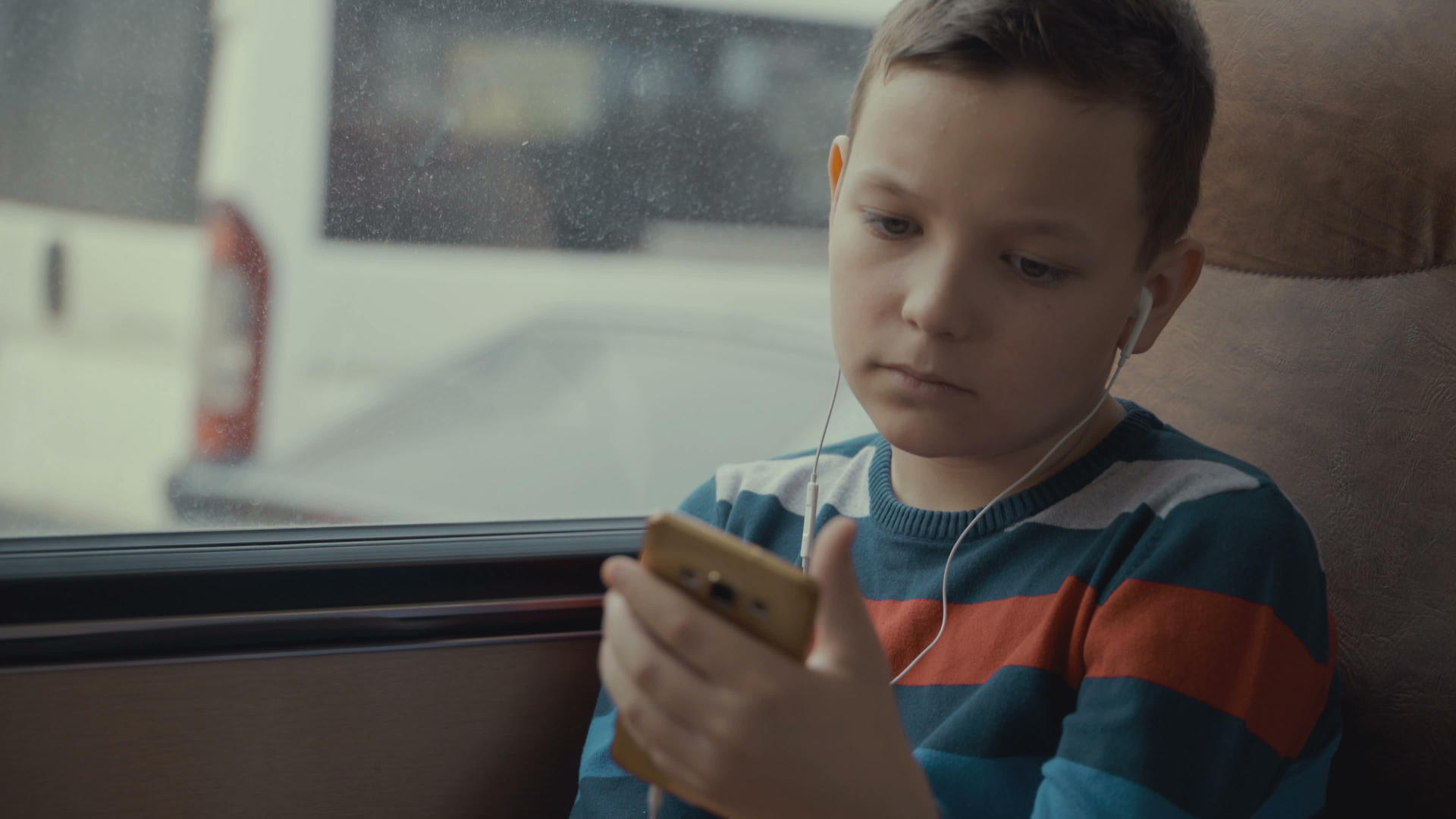 一个小男孩乘公共汽车穿越城市的特写镜头他在智能手机上视频的预览图