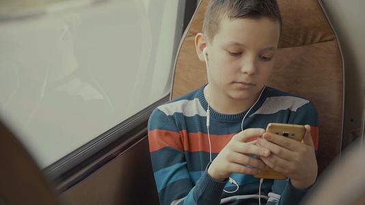 一个小男孩乘公共汽车穿越城市的特写镜头他在智能手机上视频的预览图