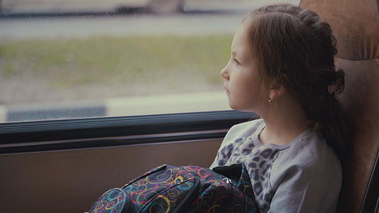 这个年轻漂亮的女孩看着窗外的窗户看着包裹在学校移动校车里的公共汽车视频的预览图