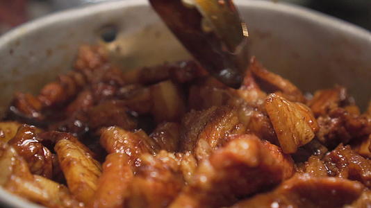 有人用勺子搅拌五花肉在锅上打滚混合棕色酱汁拍摄视频的预览图