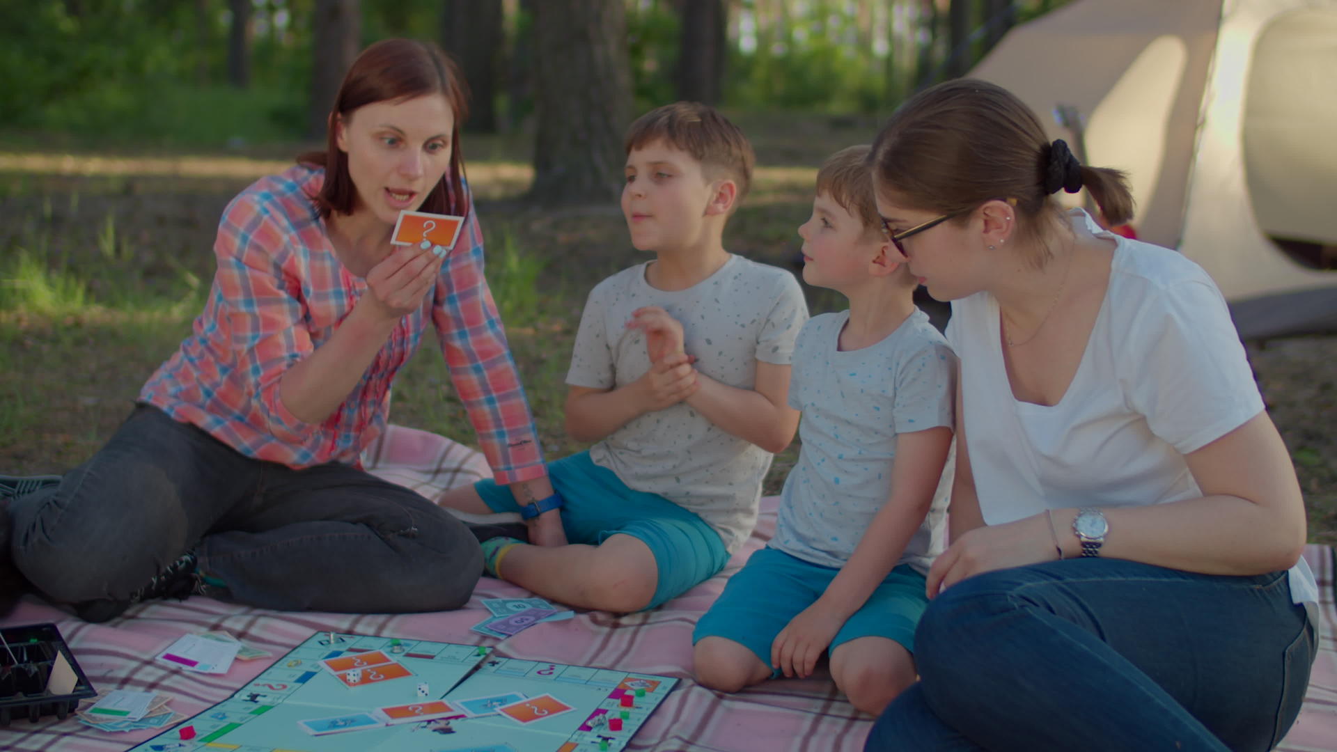 两个三十多岁的年轻母亲和两个兄弟坐在野餐毯上玩桌游视频的预览图