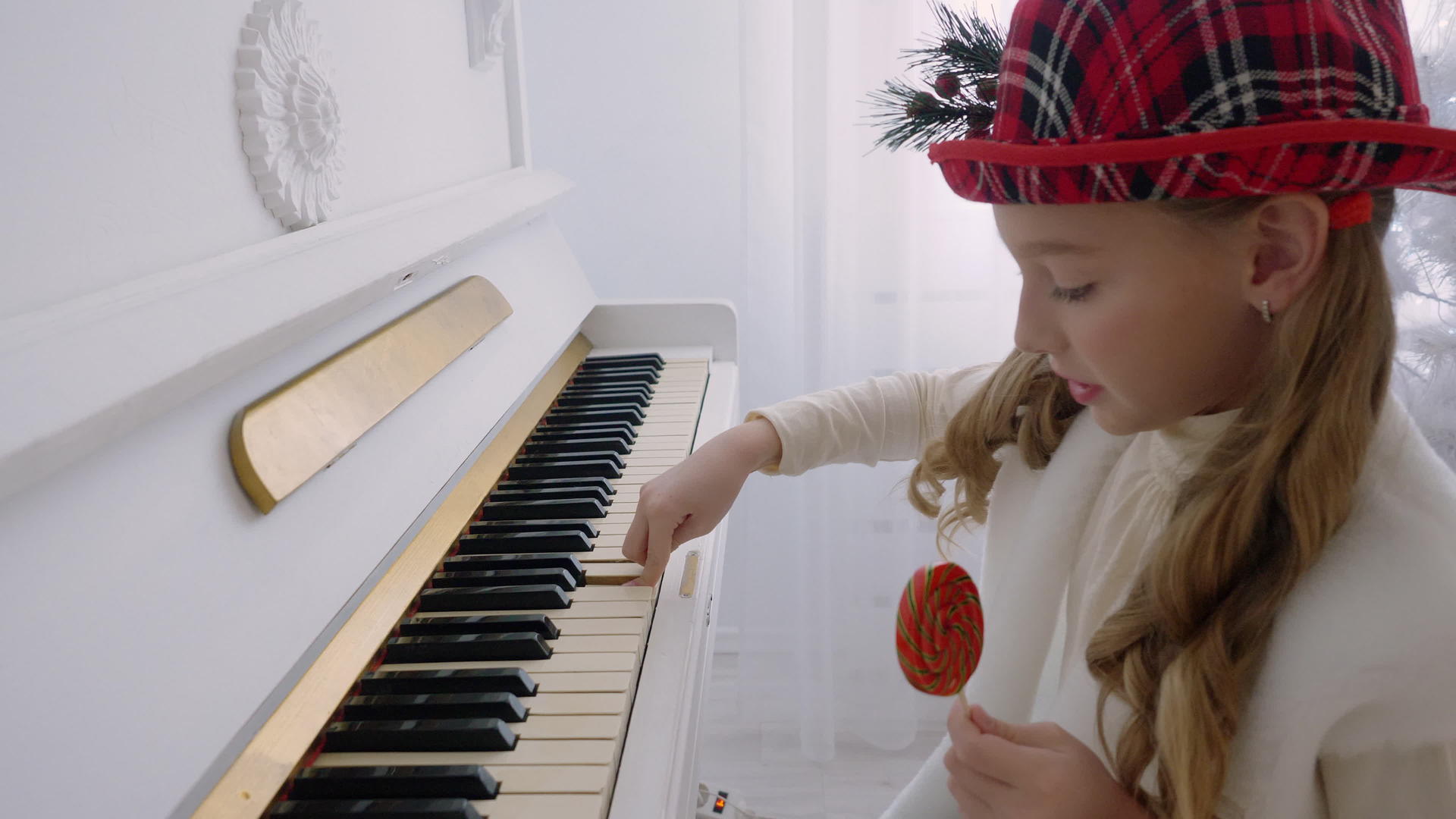 穿着红帽子的滑稽女孩在钢琴上演奏音乐手里拿着棒棒糖视频的预览图