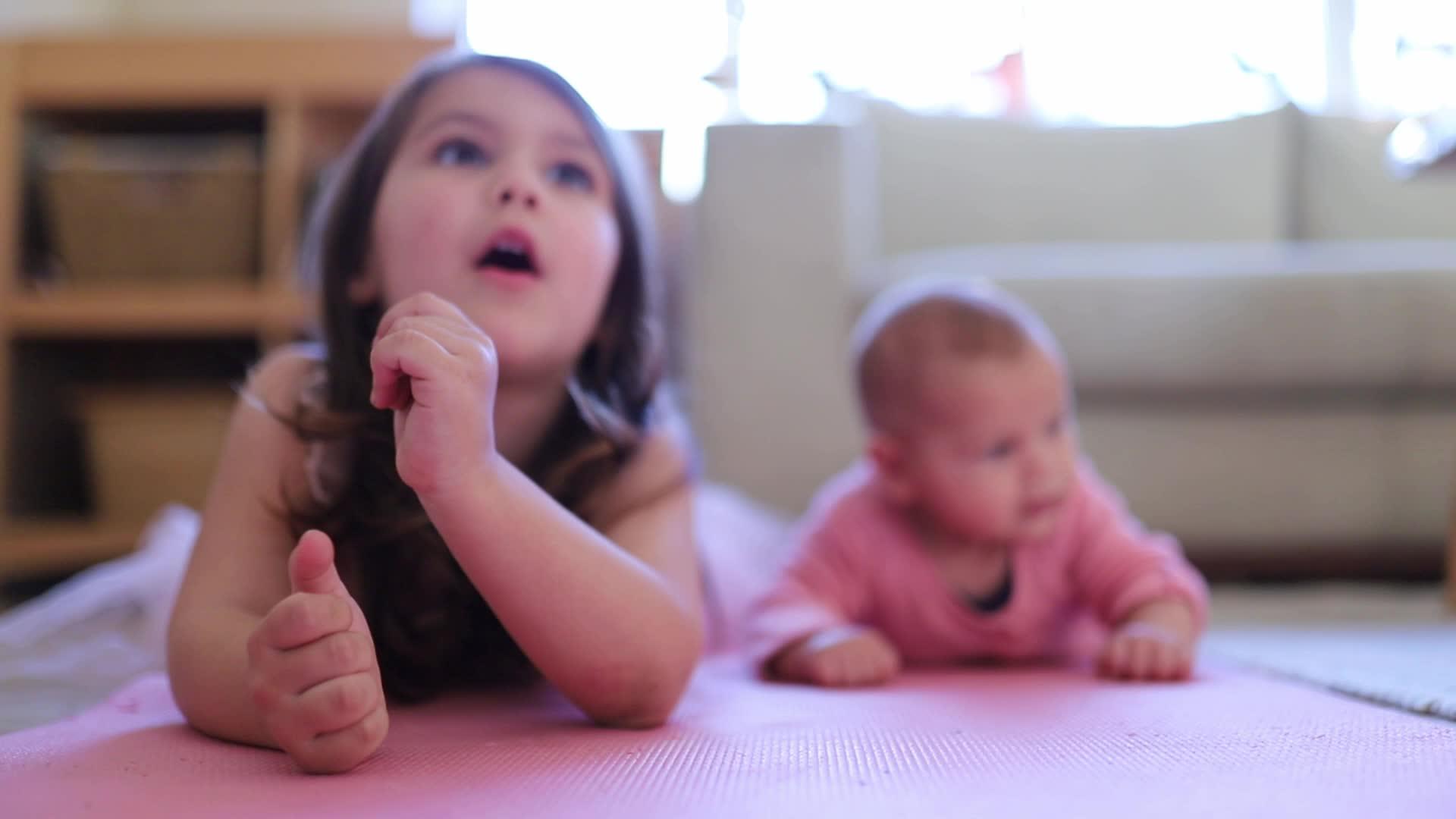 小女孩躺在她的小妹妹旁边在粉红色的地毯上视频的预览图