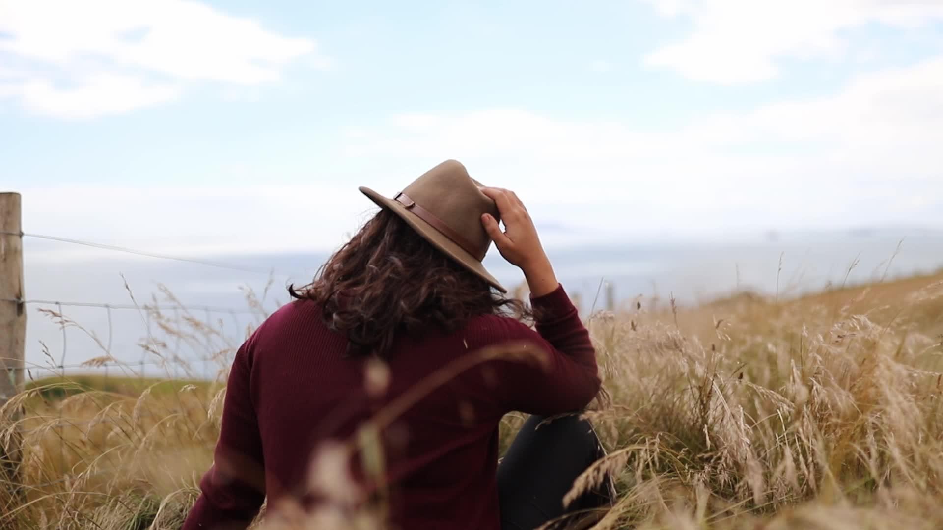 女人坐在海边的悬崖草地上吹着海风视频的预览图