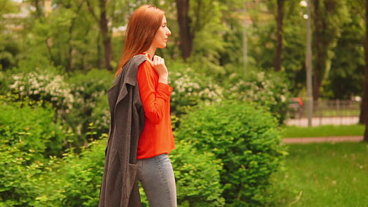 红头发的年轻女子在城市公园散步视频的预览图