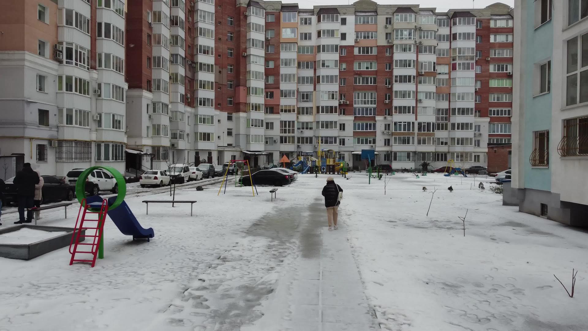 一个年轻的女人在现代房子旁边的白雪覆盖的人行道上慢慢地走着视频的预览图