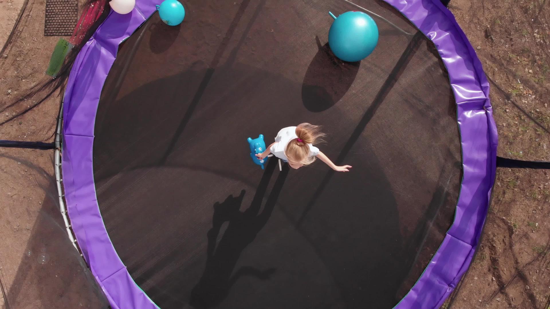 金发女孩在蹦床上跳跃在日落的顶角踢球视频的预览图