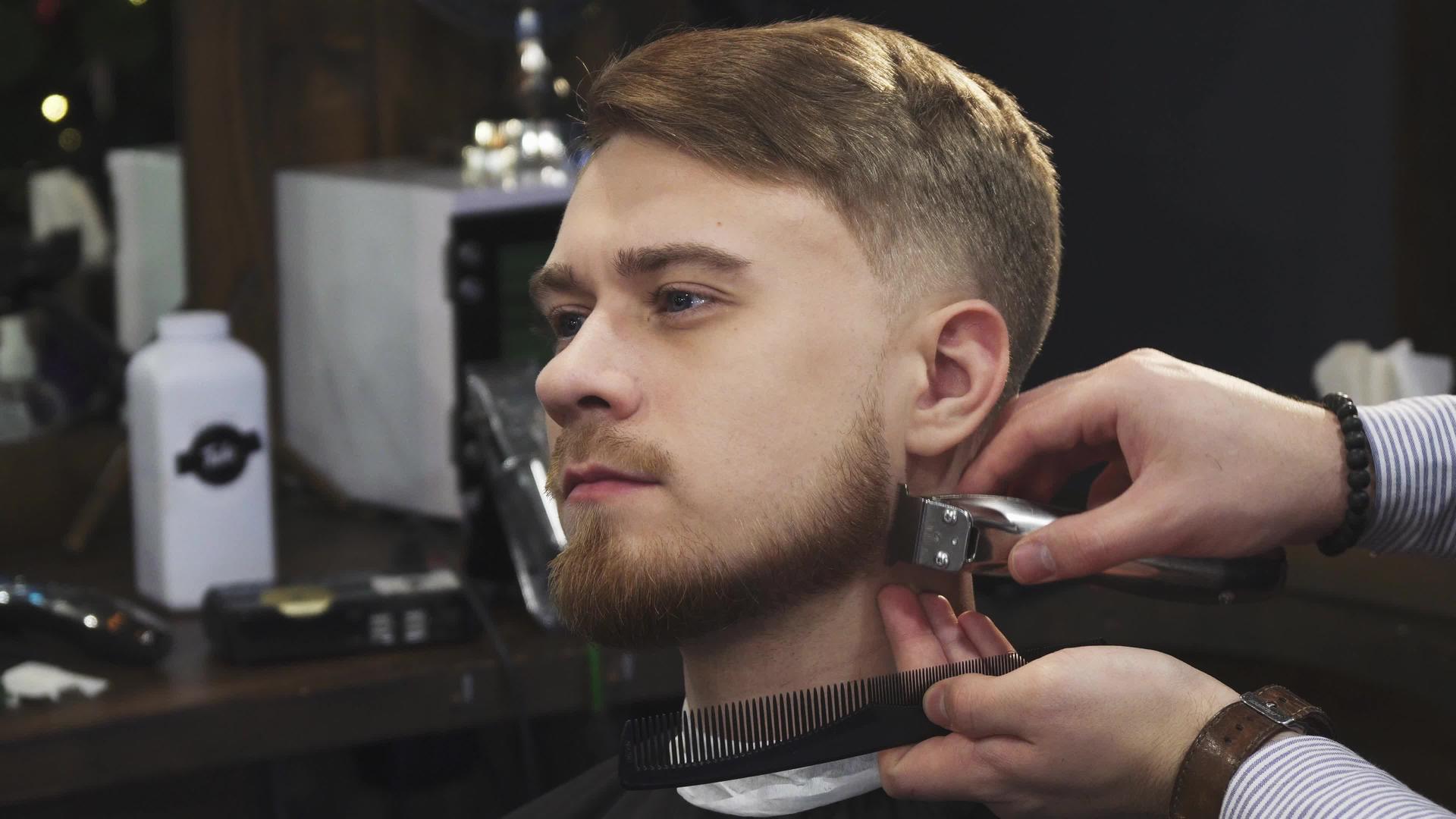 英俊的年轻帅哥被专业理发师剪胡子视频的预览图