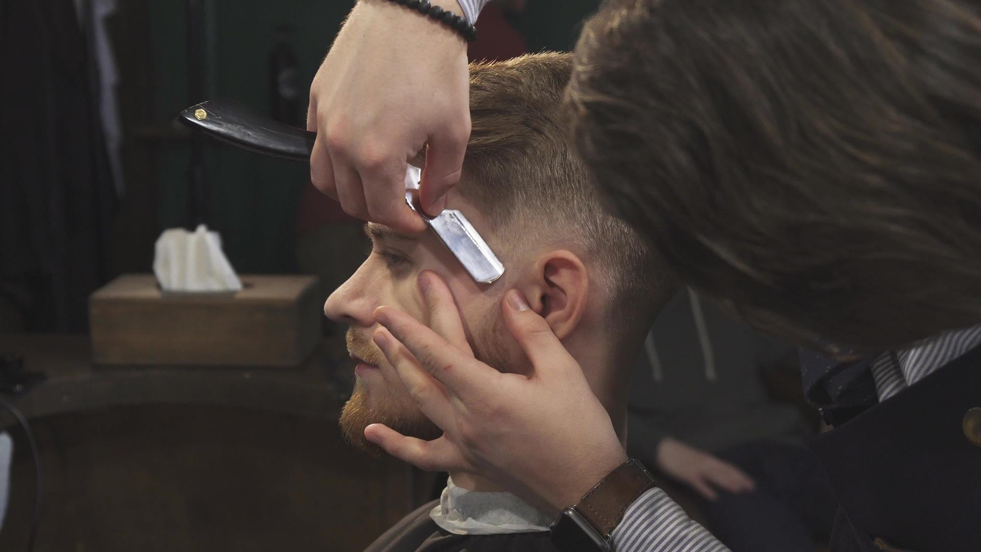 一个英俊的男人被理发师用剃刀刀剃了视频的预览图