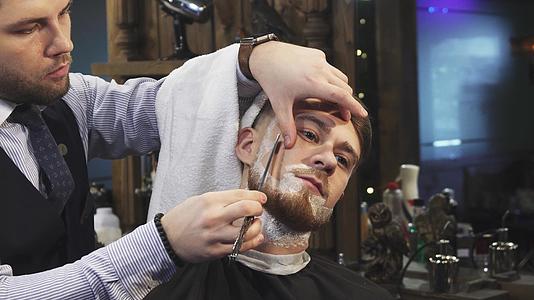 英俊的年轻人在理发店刮胡子时刮胡子视频的预览图