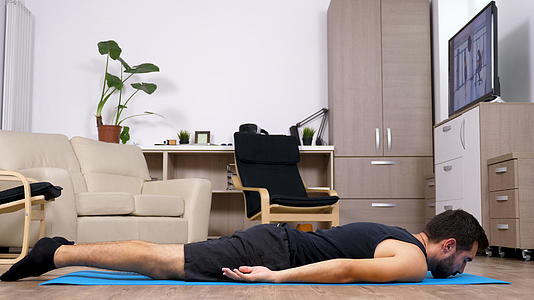 适合男人的人在客厅的蓝色垫子上做不同的瑜伽姿势视频的预览图