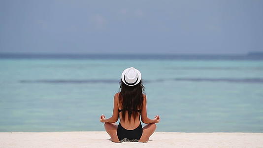 快乐放松的年轻女性在白色沙滩户外做瑜伽视频的预览图