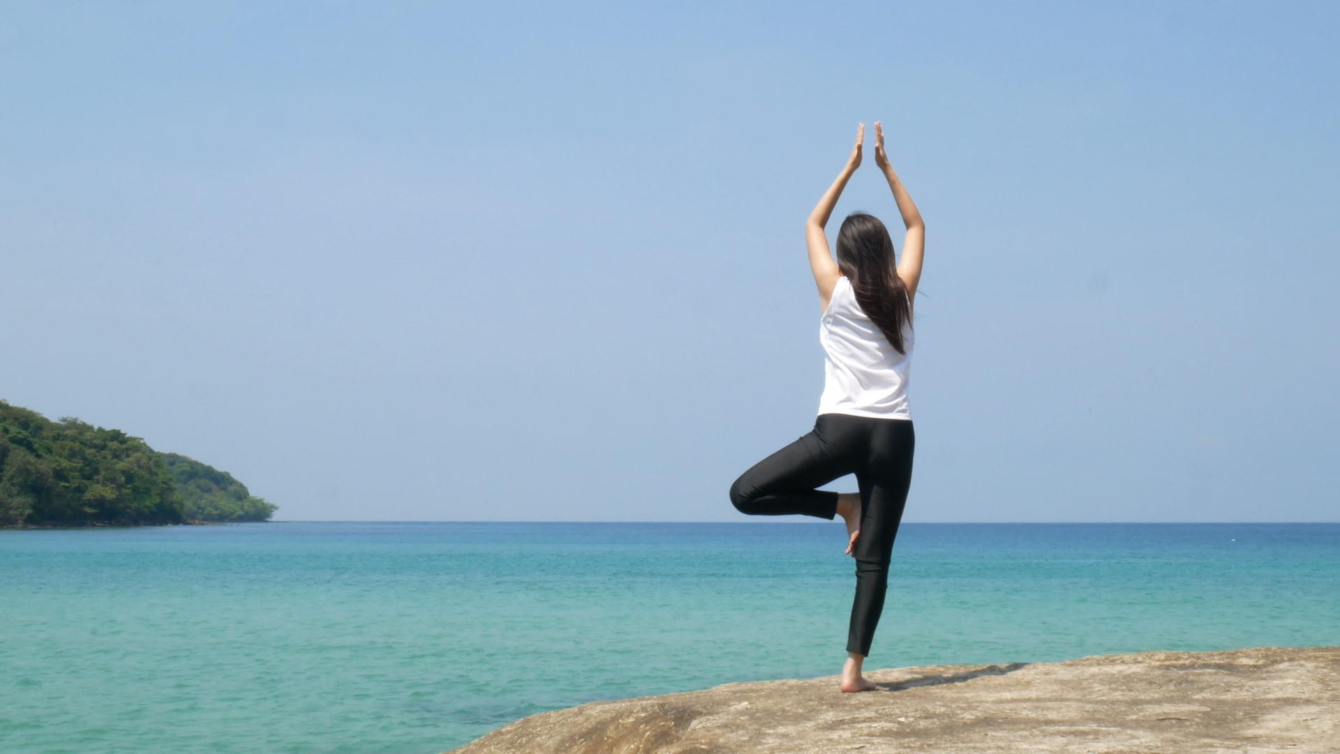 4K暑假期间一名妇女站在海边的岩石上练习瑜伽视频的预览图