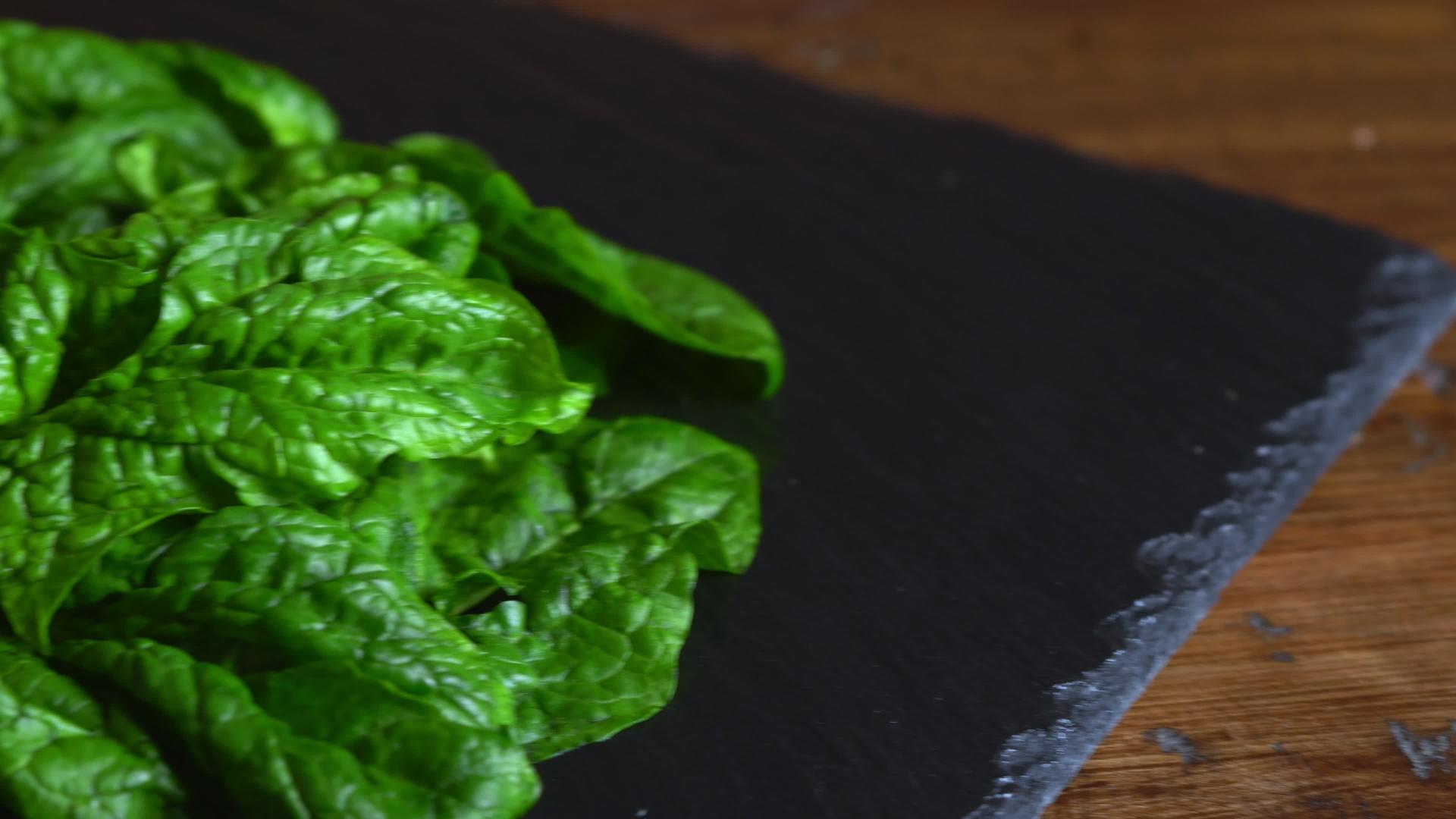 健康素食概念石板和新鲜采摘的绿色菠菜叶在木桌上的特写视频的预览图