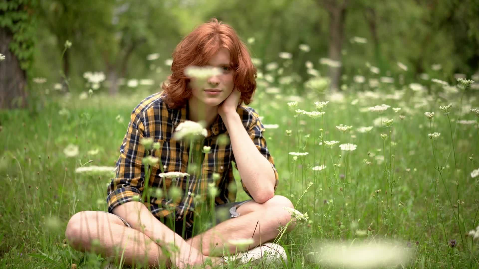 迷人的姜人坐在公园里的花里视频的预览图