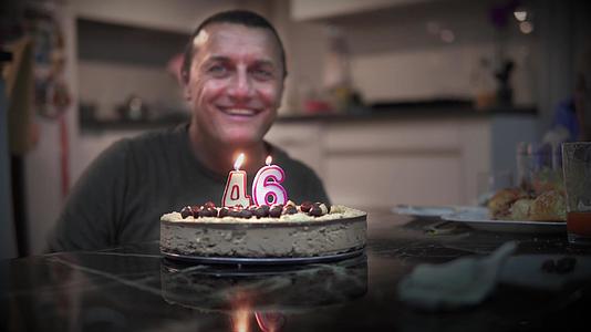 快乐的男人庆祝他46岁生日在室内自制的烤蛋糕上吹蜡烛视频的预览图