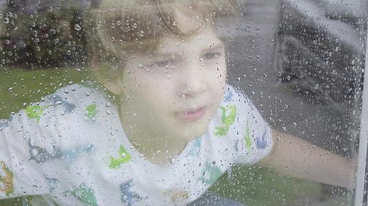 下雨天男孩从窗户往外看看着窗外视频的预览图