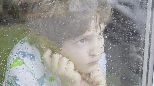 下雨天男孩从窗户往外看看着窗外视频的预览图
