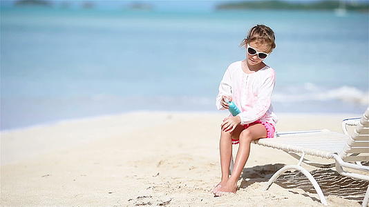 一个小女孩在热带海滩的太阳屏幕上用瓶子涂焦霜视频的预览图