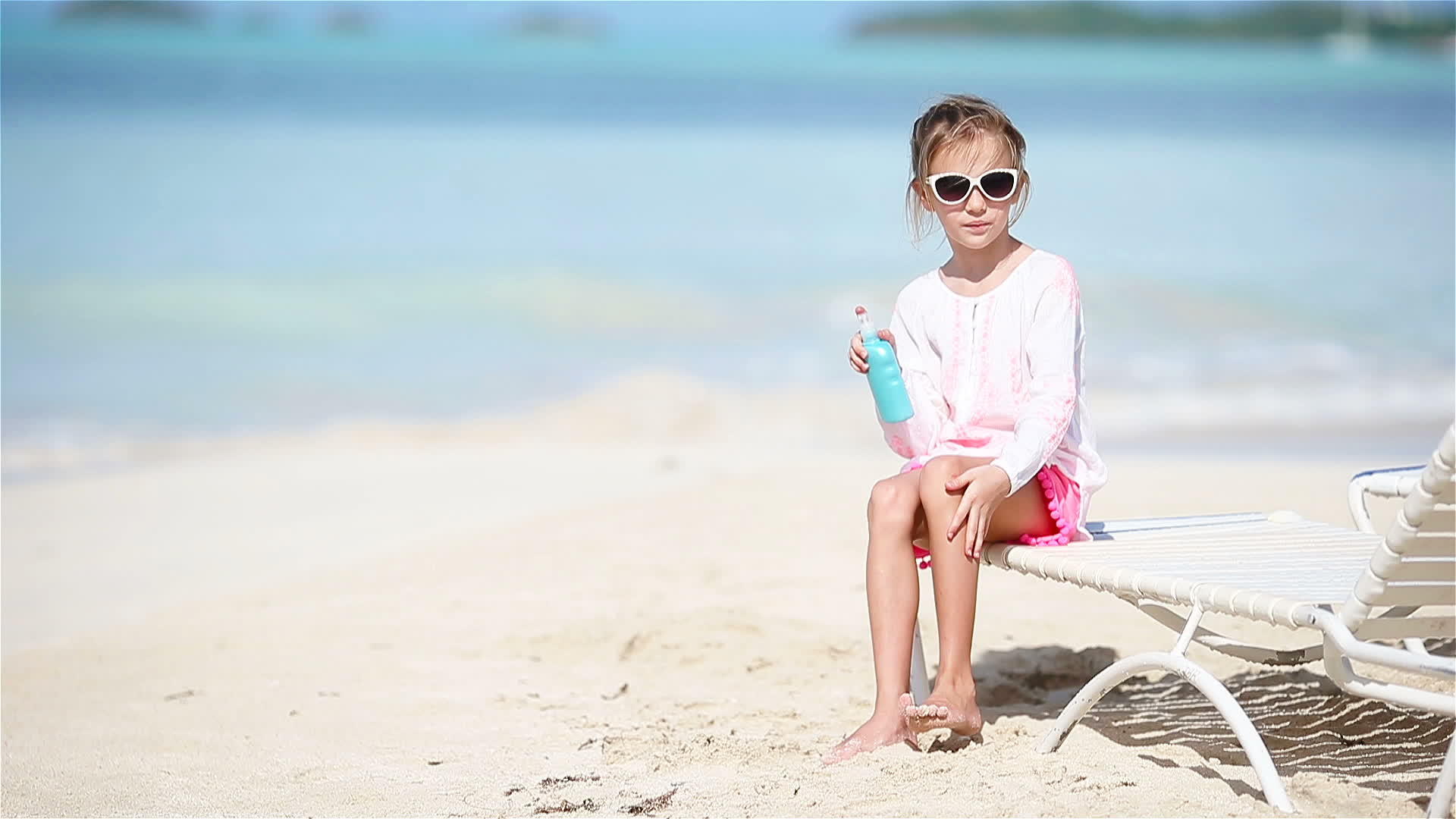 小女孩坐在热带海滩上带着一瓶防晒霜视频的预览图