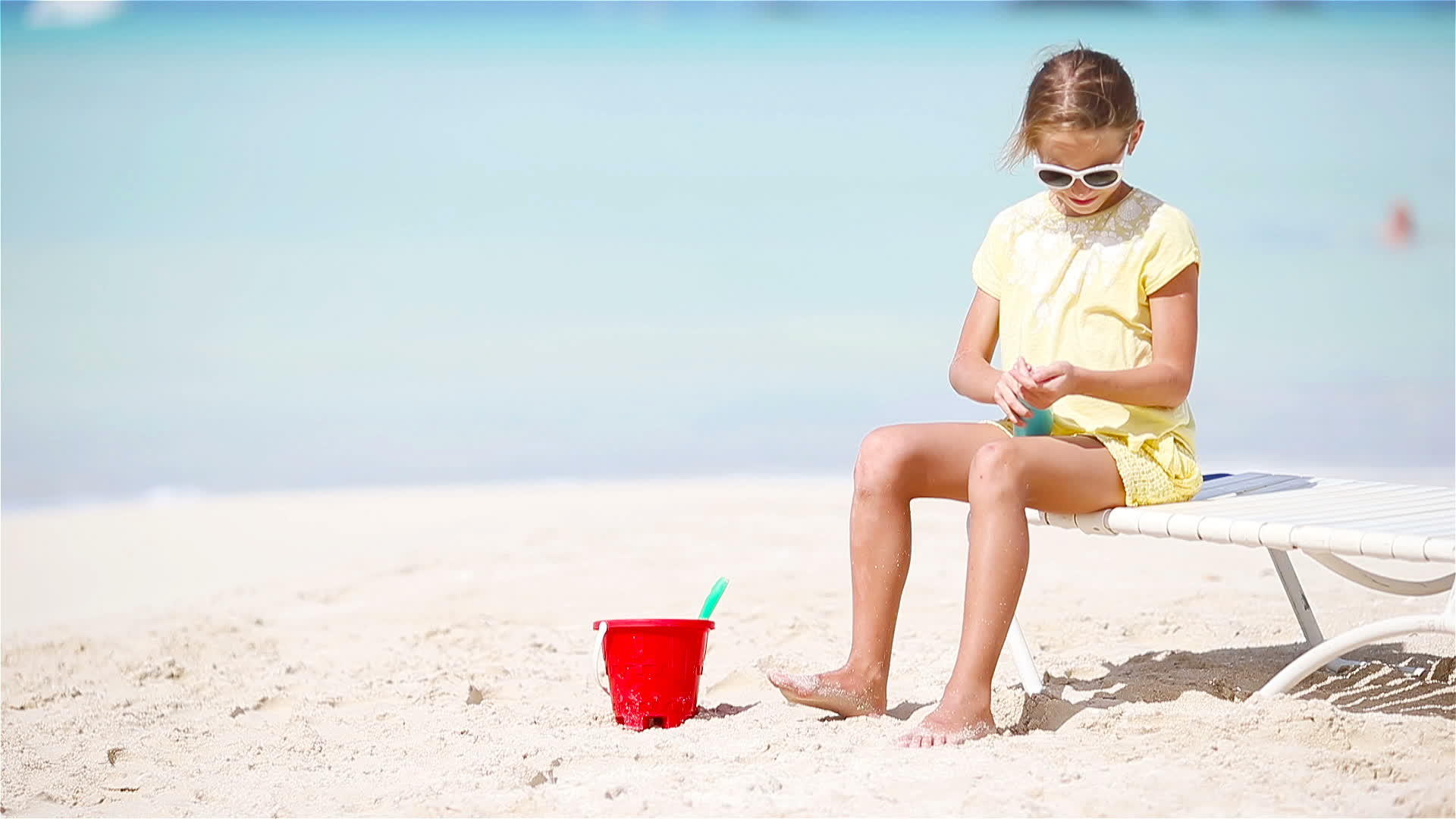 小女孩坐在热带海滩上带着一瓶防晒霜视频的预览图