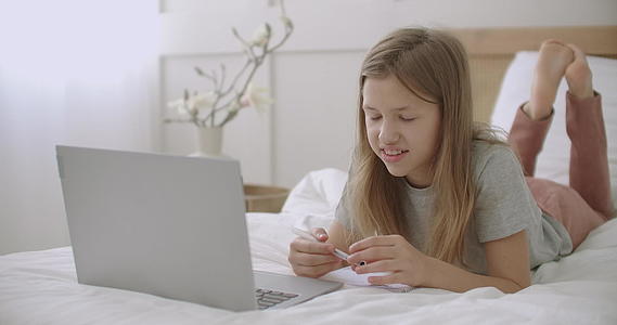 快乐的女学生在网上课程中通过笔记本电脑回答躺在床上视频的预览图