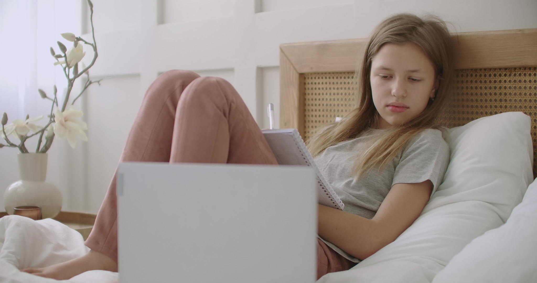 疲惫无聊的女学生躺在床上在笔记本电脑上有一本练习本视频的预览图