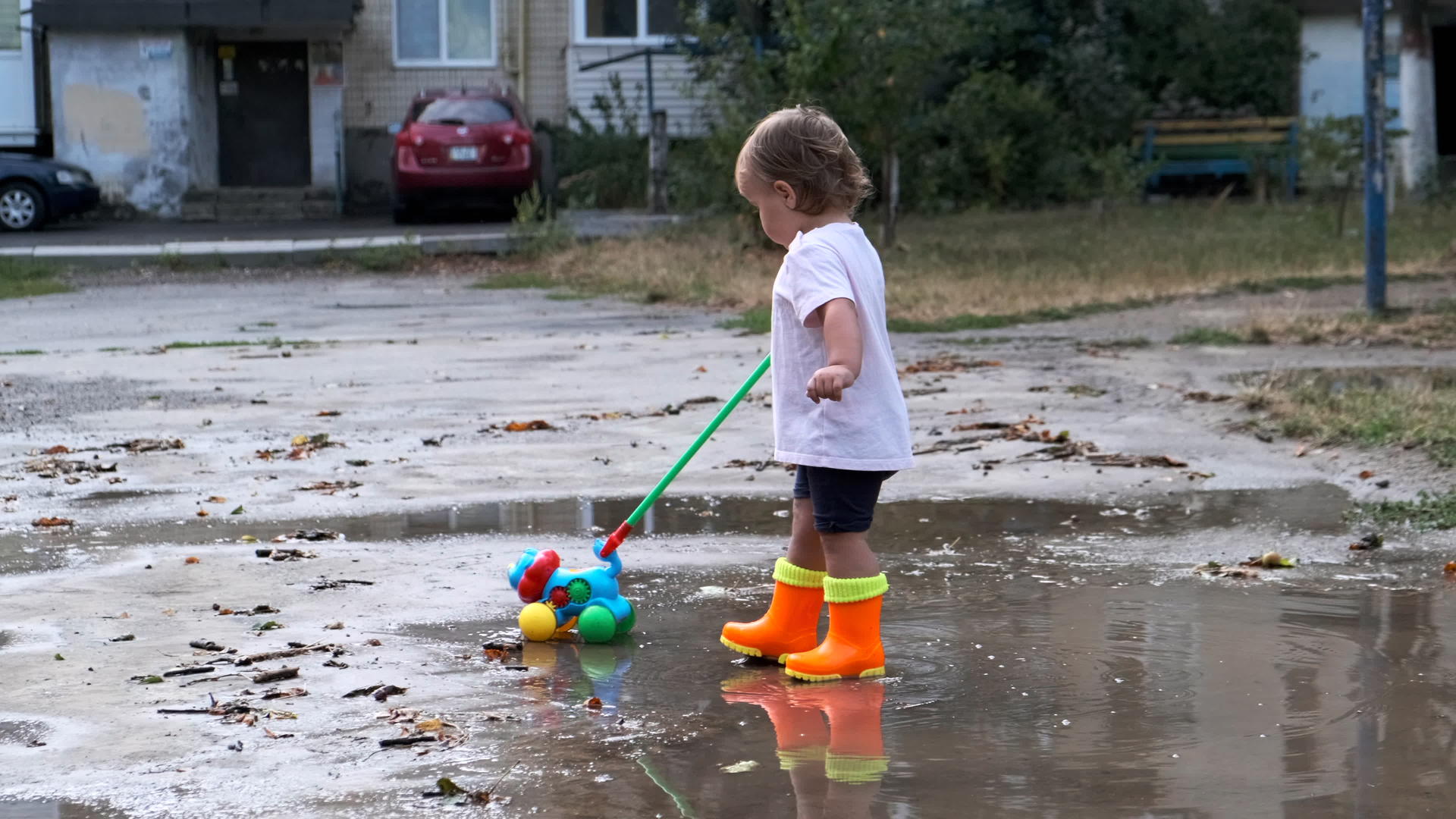 雨后一个穿着橙色靴子的孩子拉着玩具穿过水坑视频的预览图