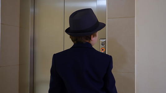 小男孩穿着西装、帽子和公文包进入电梯商人按下按钮视频的预览图
