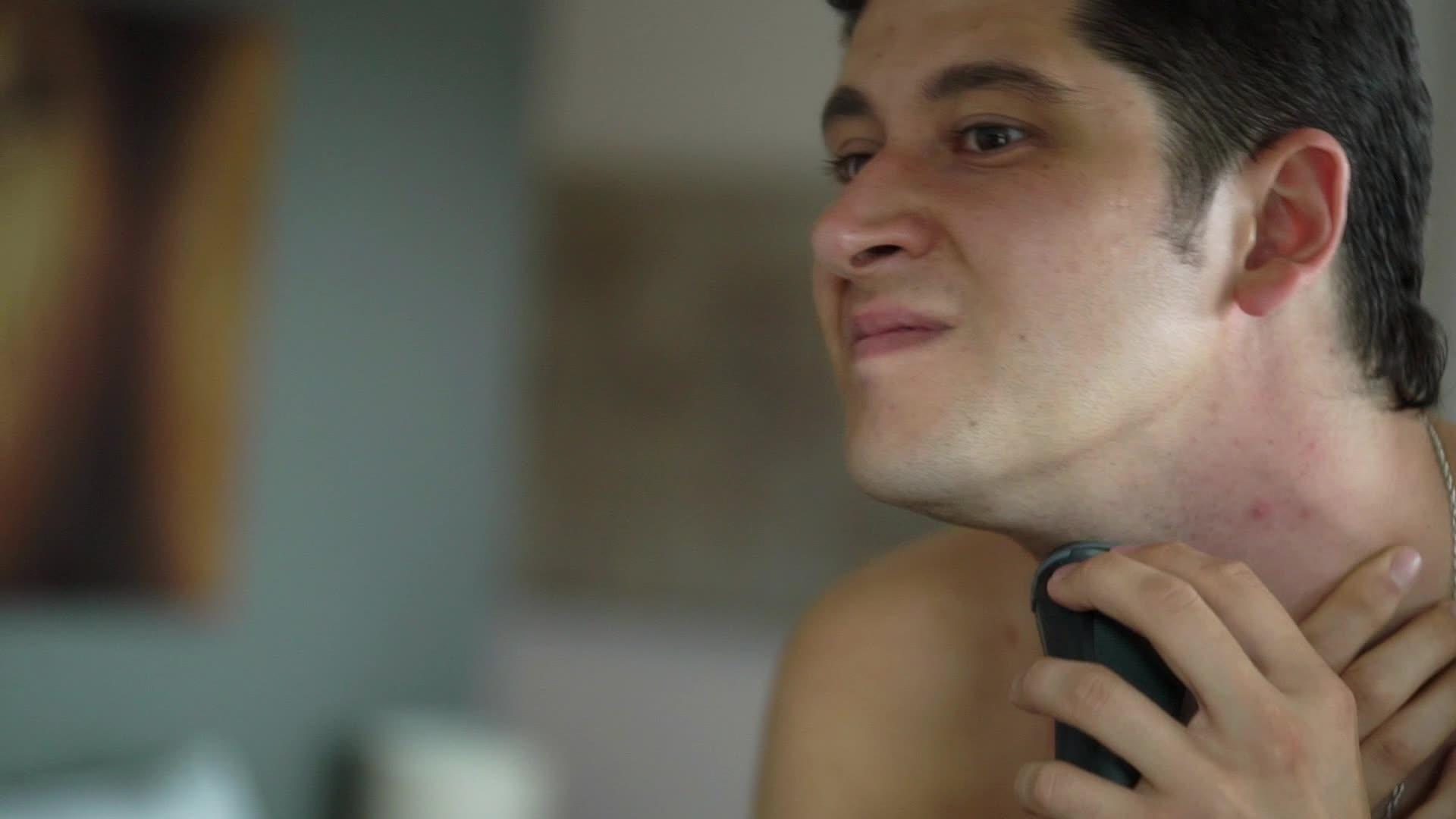 英俊的年轻人在浴室里剃须刀和电剃刀靠近镜子视频的预览图