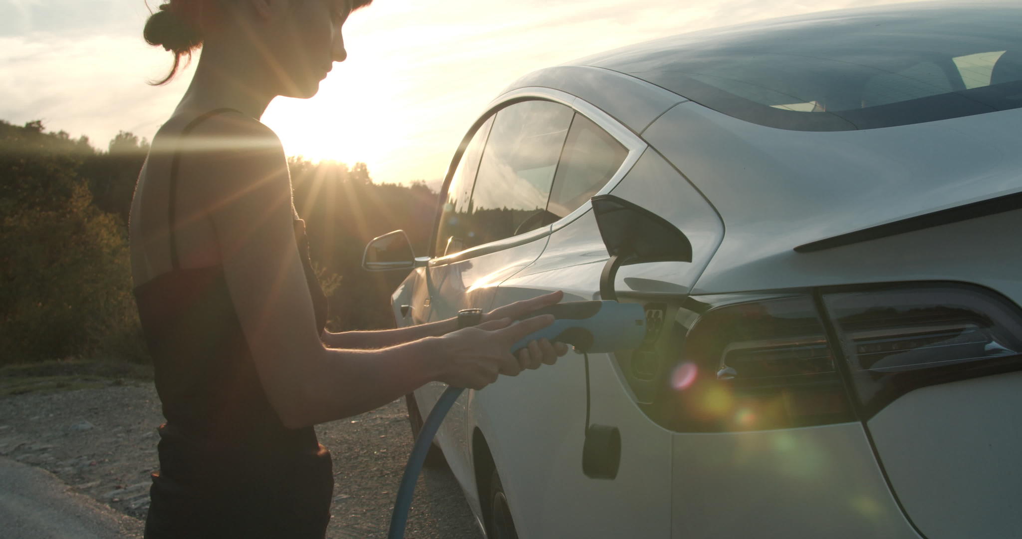 日落时女孩在电动汽车上插上充电电缆视频的预览图