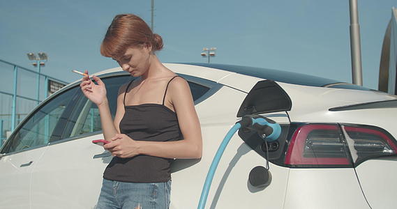 女孩抽雪茄看电话她的电动车正在充电视频的预览图