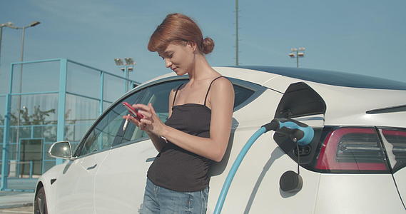 女孩在电动汽车充电时用智能手机吸烟和自拍视频的预览图