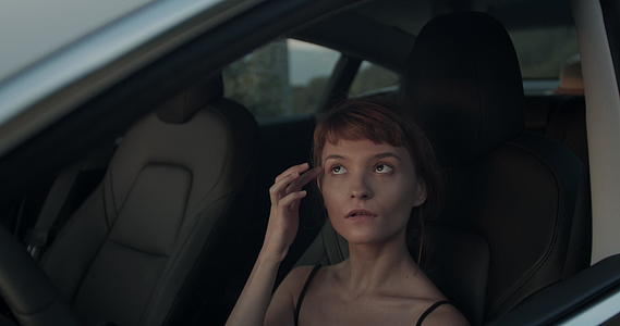 一个穿着电动汽车的可爱女孩看着她的头发和镜子里的化妆手视频的预览图