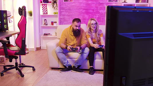 一对兴奋的年轻夫妇坐在沙发上玩电子游戏视频的预览图