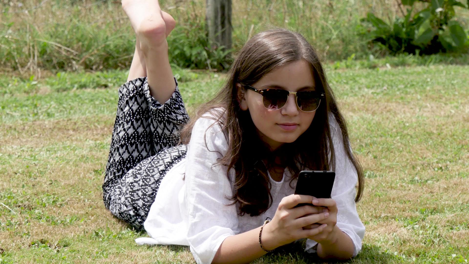 躺在草地上的女孩正在使用智能手机视频的预览图